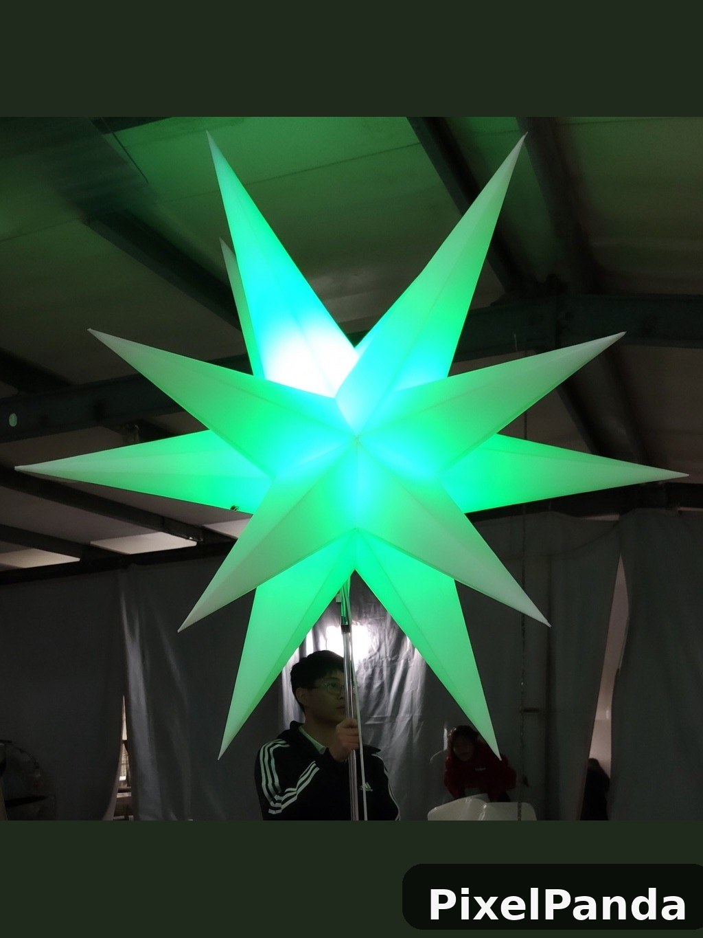 Glowing green star sculpture indoors with person beneath