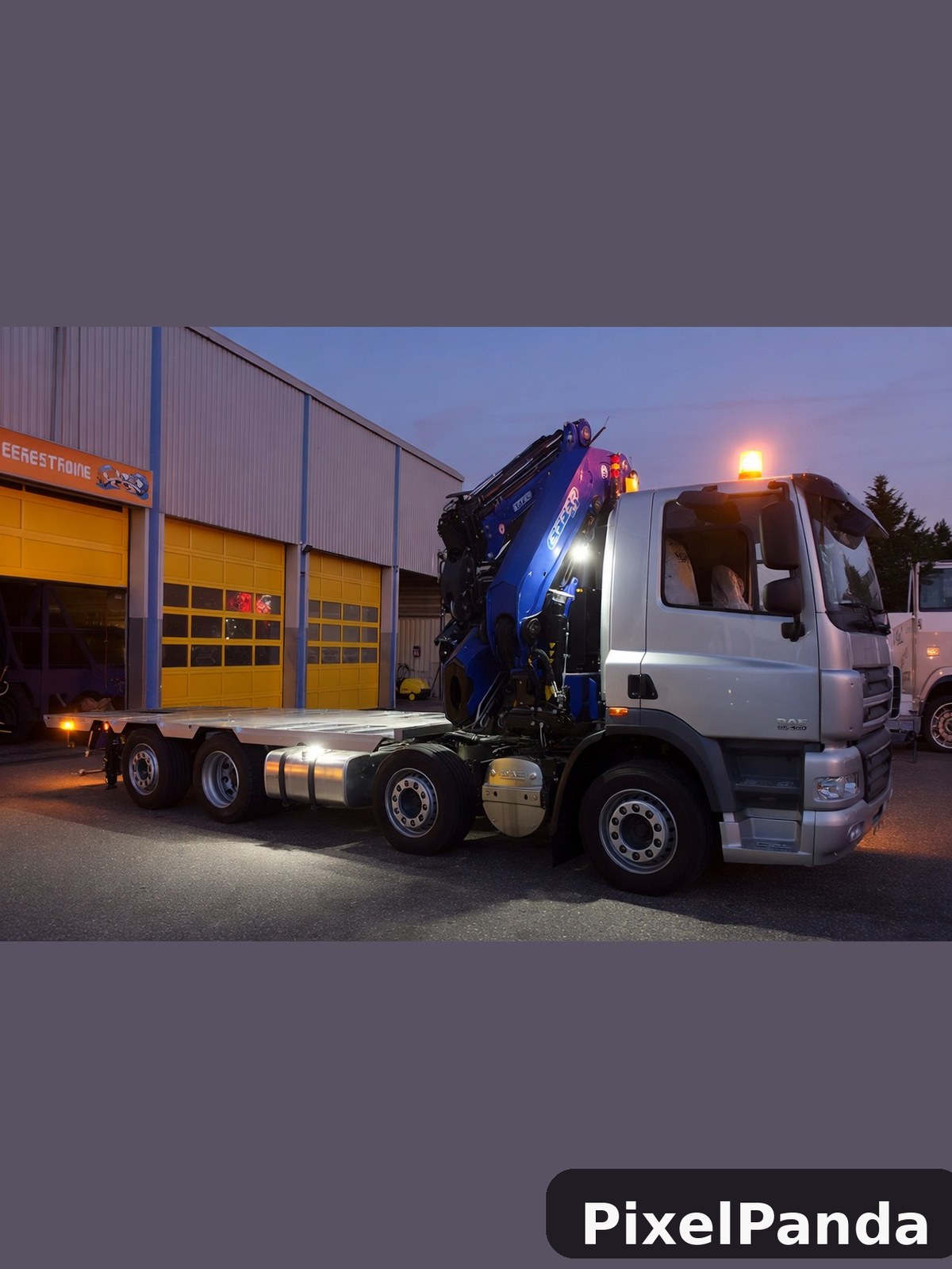 Silver flatbed truck with blue hydraulic crane at dusk