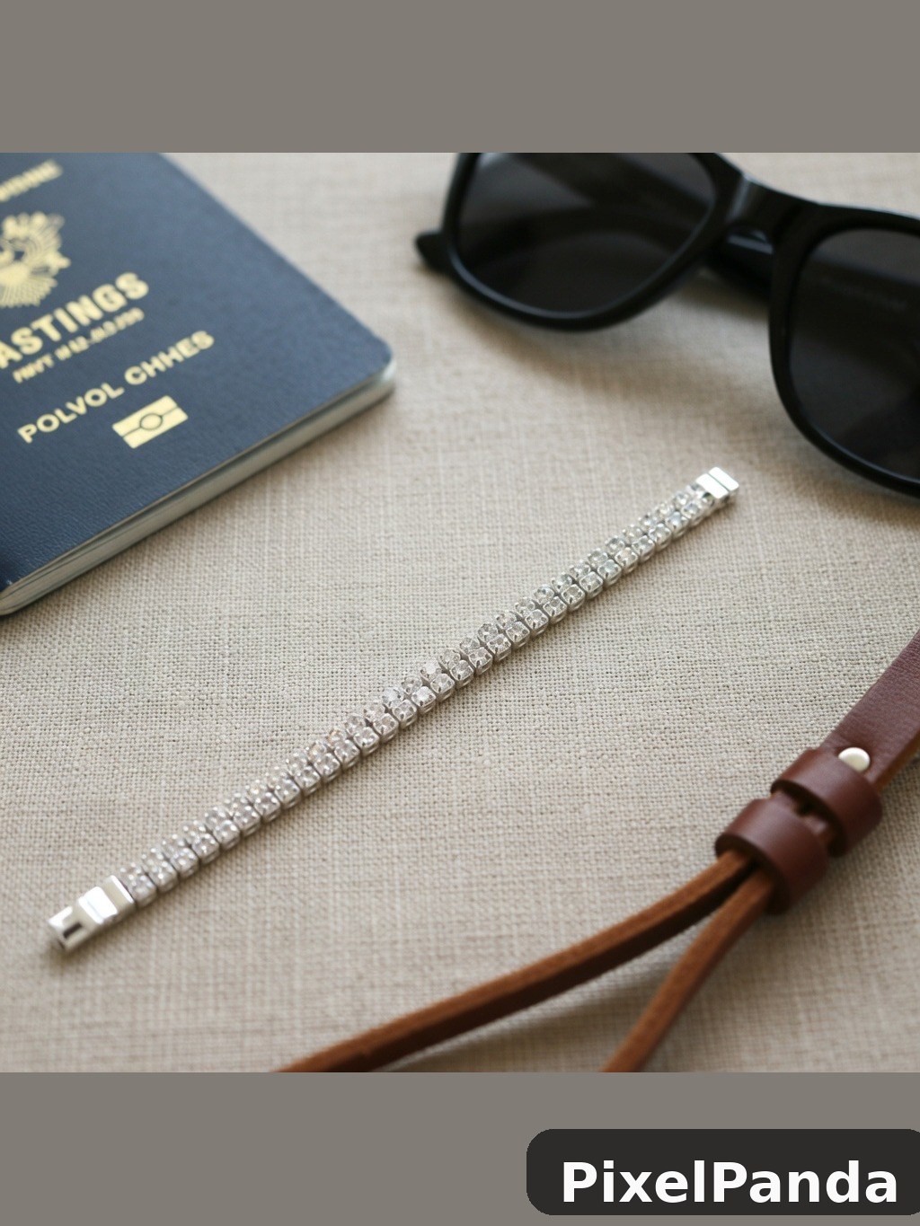 Diamond tennis bracelet with passport and sunglasses on beige linen