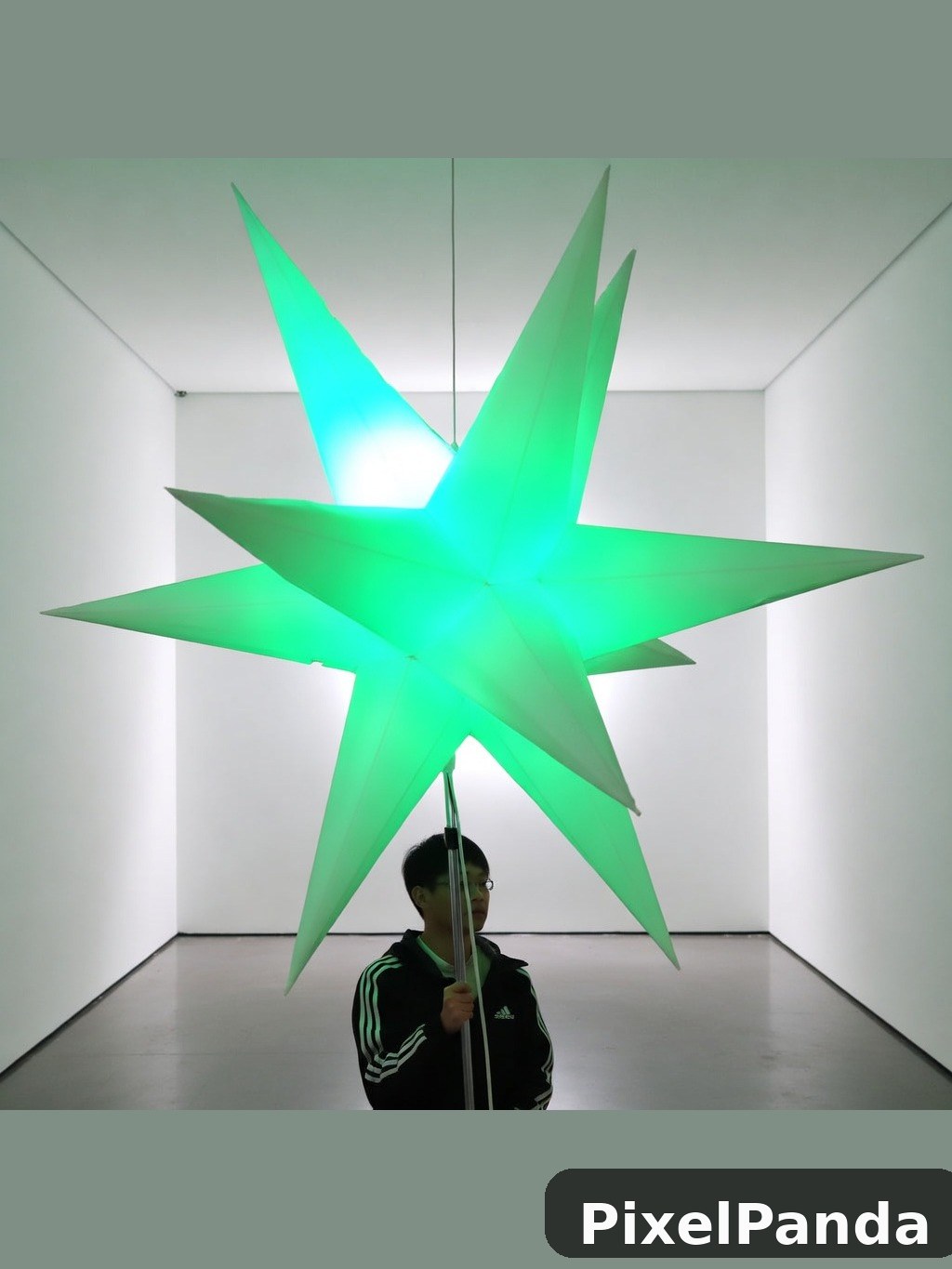 Person standing beneath glowing green star sculpture in white gallery