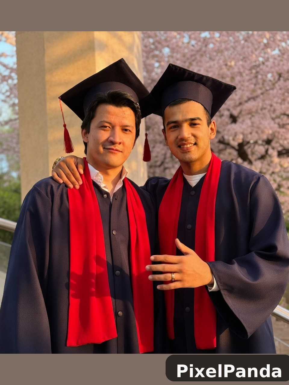 Two graduates in navy robes and red stoles with caps and tassels