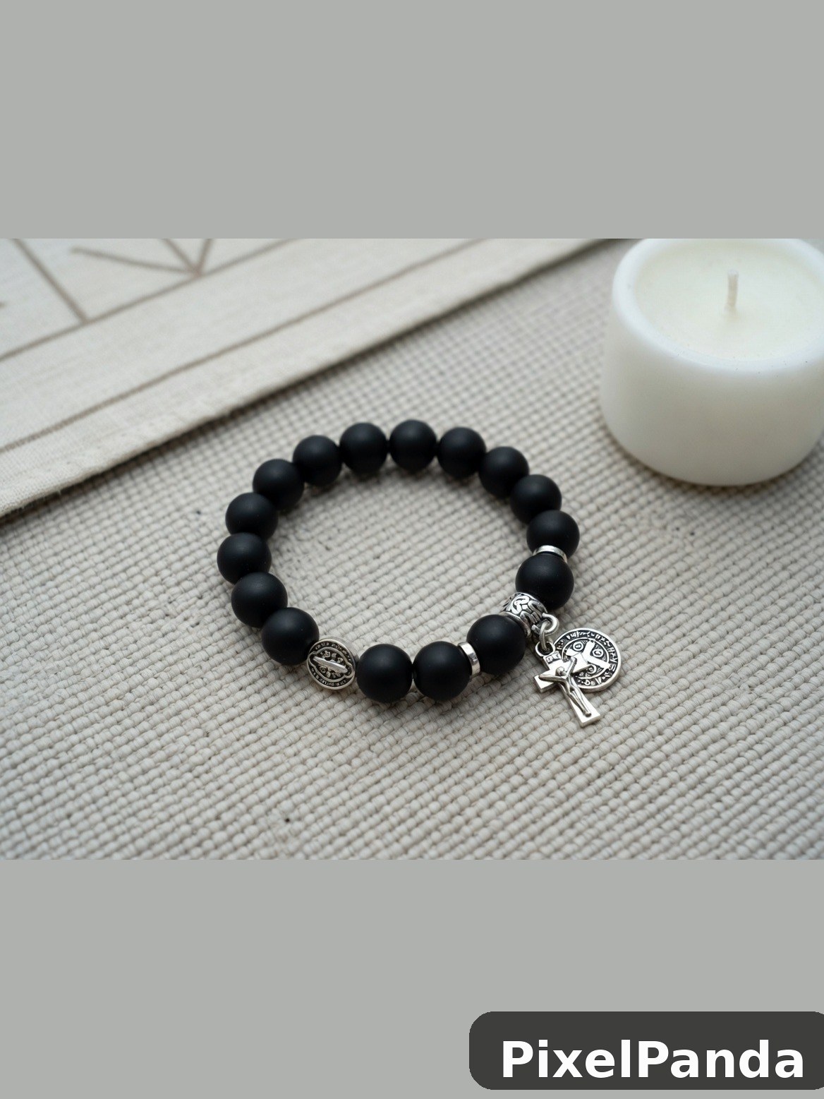 Black beaded bracelet with silver cross charm on neutral fabric