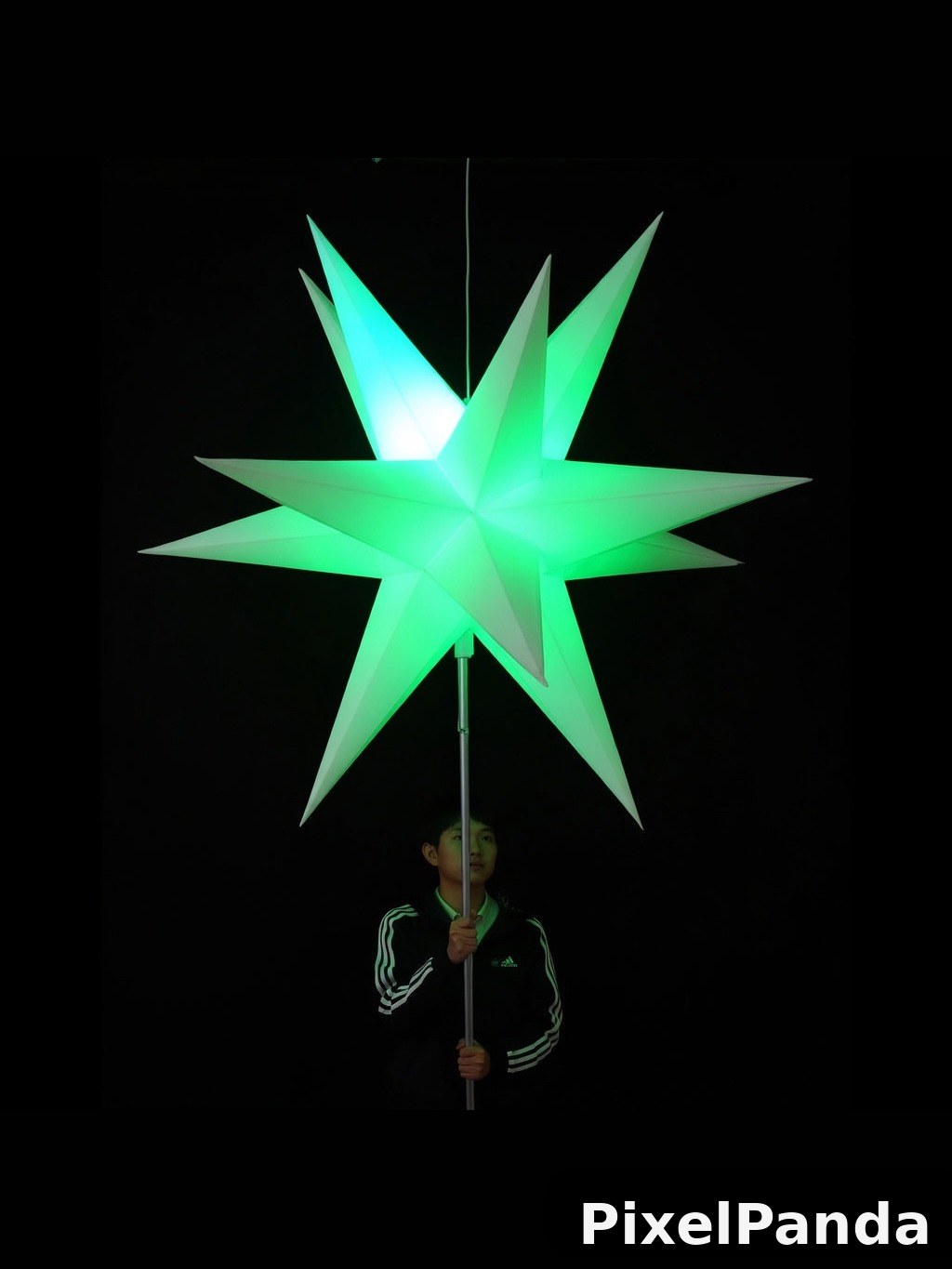 Child holding illuminated green star lantern against black background
