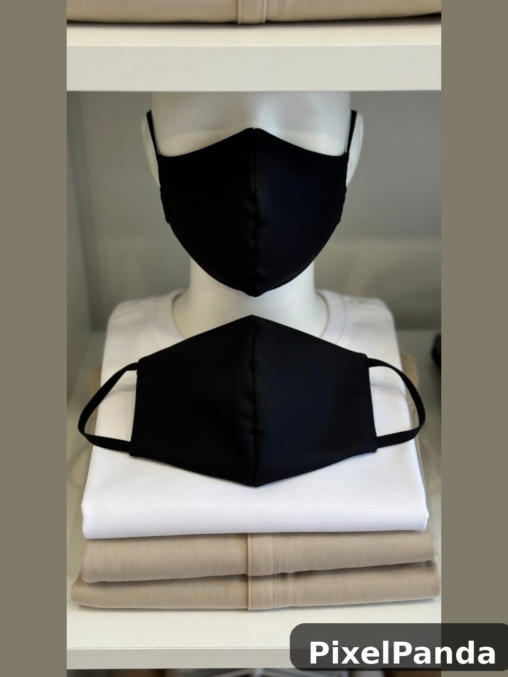 Two black fabric masks displayed on white and beige folded clothing