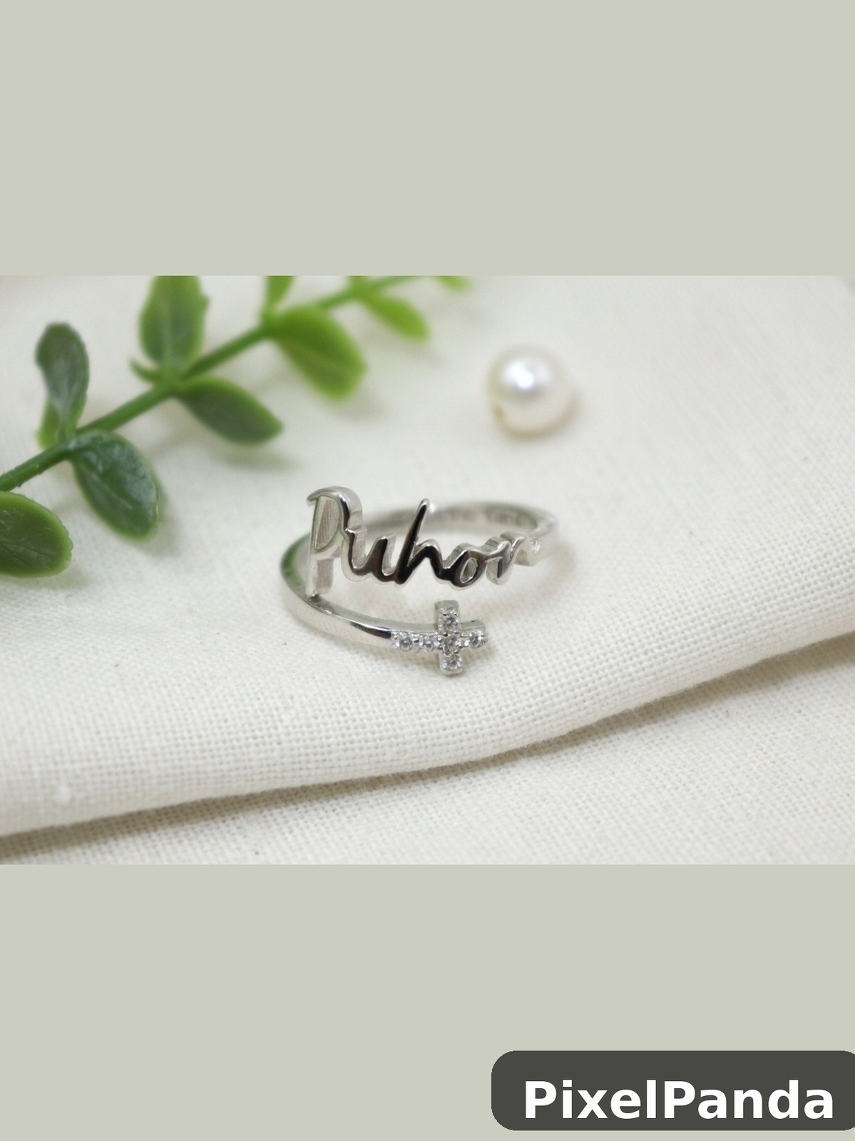 Silver name ring with cross charm on cream fabric
