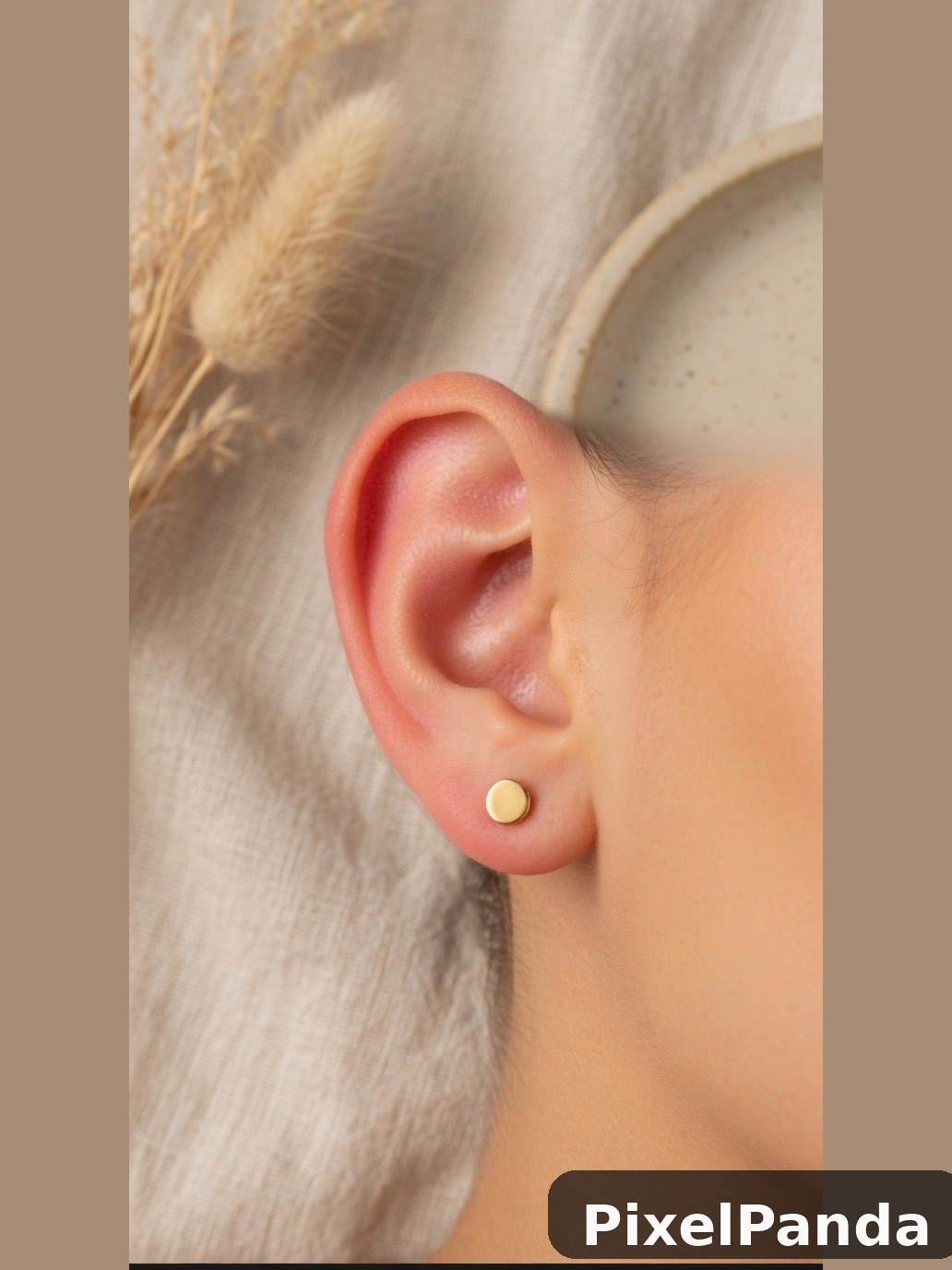 Small gold stud earring on ear with neutral linen background