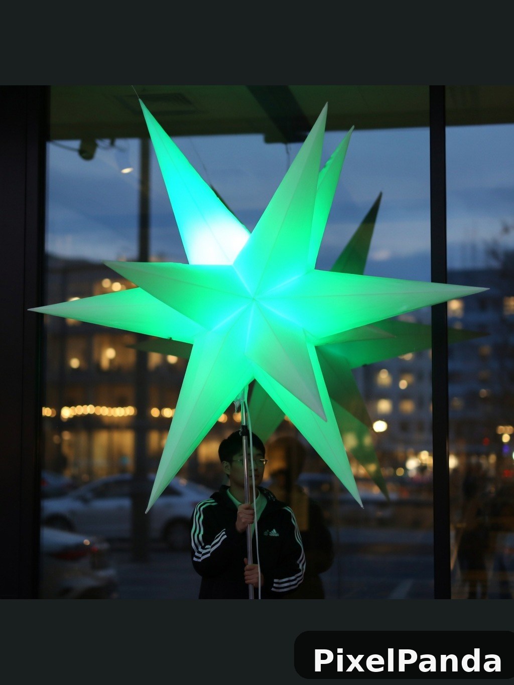 Person holding illuminated green star decoration at dusk