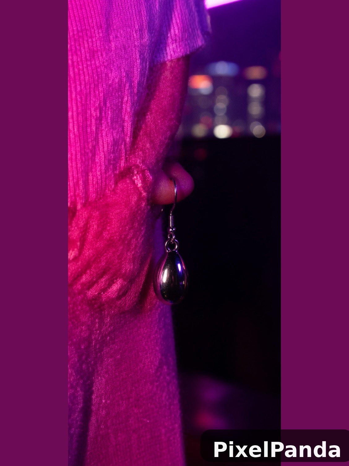 Person in hot pink ribbed sweater wearing dark teardrop earring